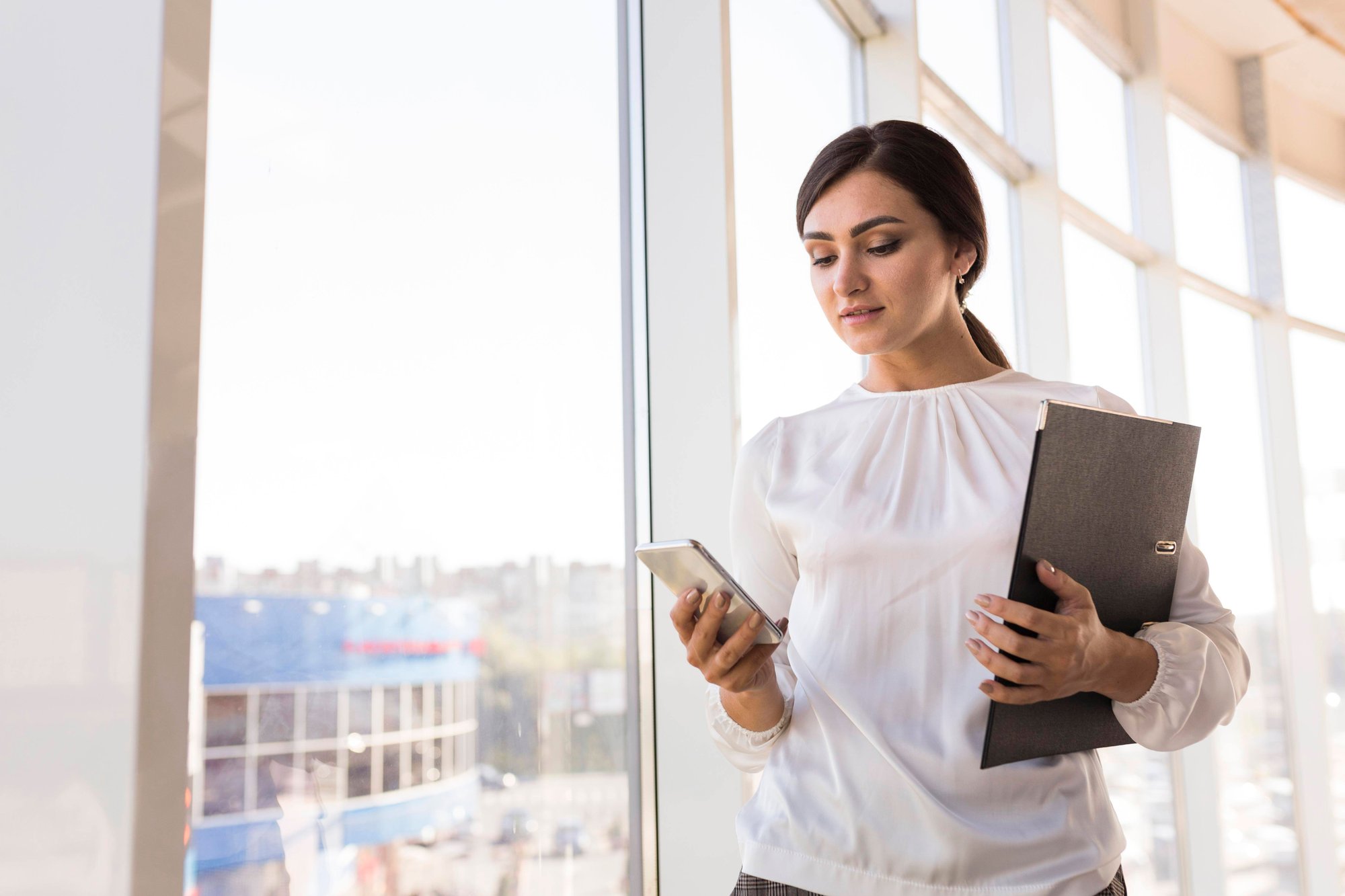 business-woman-holding-binder-looking-smartphone business-woman-holding-binder-looking-smartphone